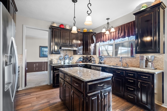 kitchen with under cabinet range hood, a kitchen island, a sink, appliances with stainless steel finishes, and decorative light fixtures