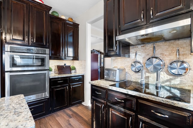 kitchen featuring stainless steel double oven, under cabinet range hood, black electric stovetop, and light stone countertops