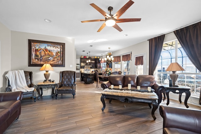 living area with ceiling fan with notable chandelier, wood finished floors, and a wealth of natural light