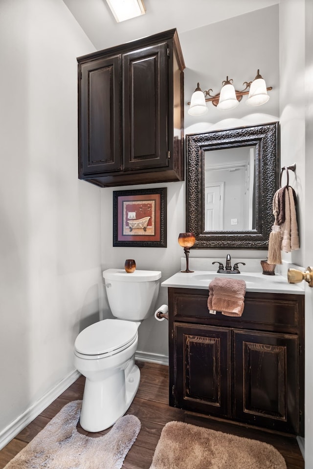 bathroom featuring toilet, baseboards, wood finished floors, and vanity