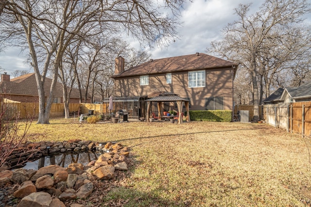 back of property with a fenced backyard, a chimney, and a gazebo