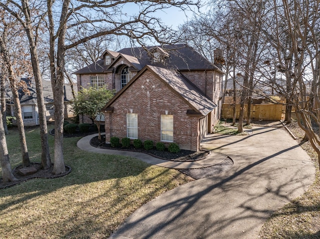 view of property exterior with a yard, driveway, brick siding, and fence