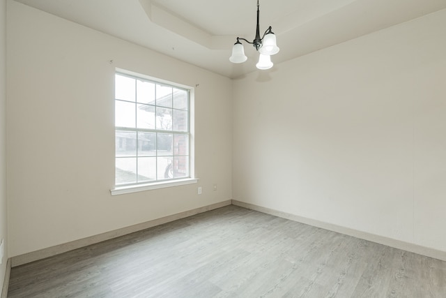 empty room with a tray ceiling, light hardwood / wood-style flooring, and a chandelier