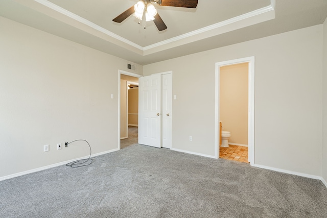 unfurnished bedroom featuring ceiling fan, light carpet, ensuite bathroom, and a raised ceiling