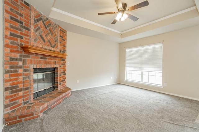 unfurnished living room with ceiling fan, a brick fireplace, a tray ceiling, carpet flooring, and ornamental molding