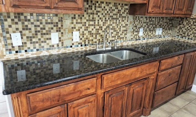 kitchen featuring light tile patterned floors, tasteful backsplash, dark stone counters, brown cabinetry, and a sink