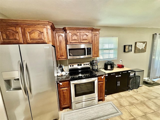 kitchen with light tile patterned floors, appliances with stainless steel finishes, dark countertops, and brown cabinets