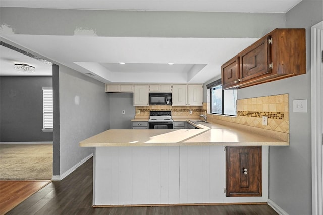 kitchen featuring kitchen peninsula, decorative backsplash, a raised ceiling, and range with electric cooktop