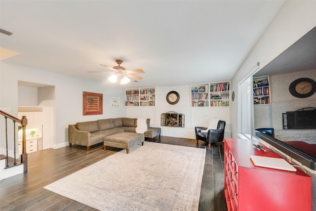 living room with ceiling fan, a fireplace, dark hardwood / wood-style floors, and built in shelves