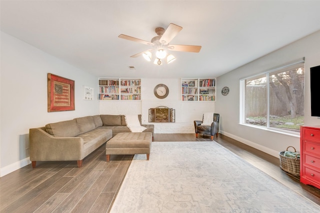 living room with ceiling fan, built in shelves, a fireplace, and hardwood / wood-style flooring