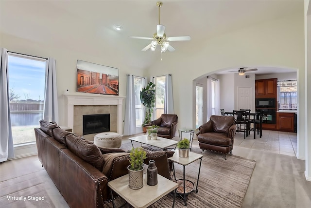 tiled living room featuring ceiling fan, a tiled fireplace, and a high ceiling