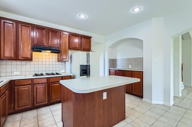 kitchen featuring a center island, decorative backsplash, gas cooktop, light tile patterned flooring, and white refrigerator with ice dispenser