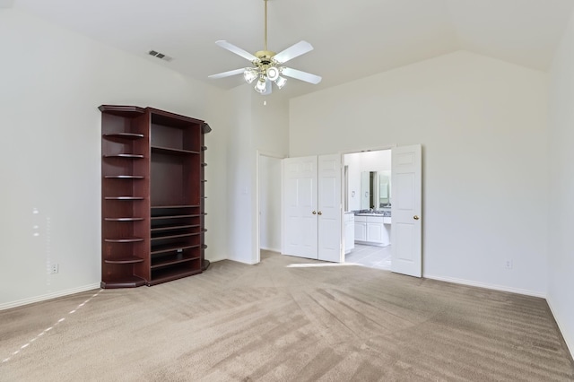 unfurnished bedroom with ceiling fan, light colored carpet, high vaulted ceiling, and ensuite bath