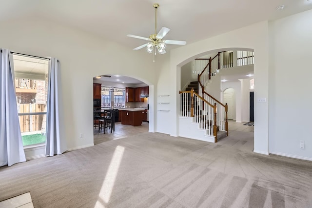 unfurnished living room with ceiling fan, light colored carpet, and a towering ceiling