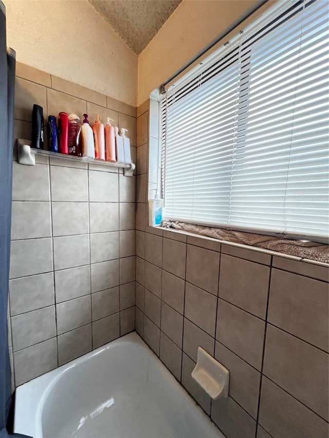 bathroom with a textured ceiling and a tub to relax in