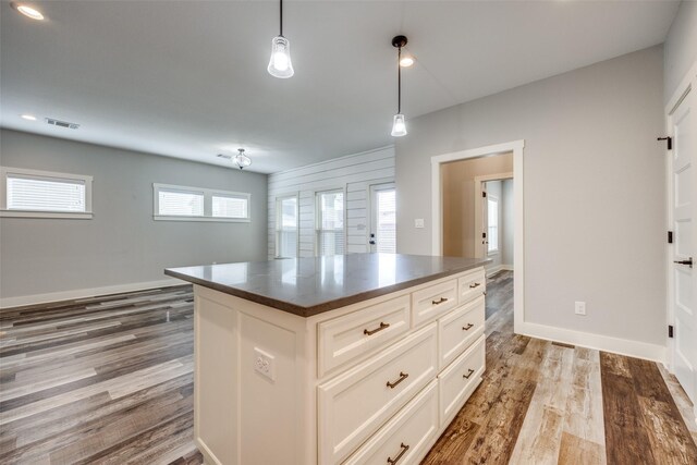 kitchen with stainless steel appliances, decorative light fixtures, dark stone counters, white cabinets, and a center island