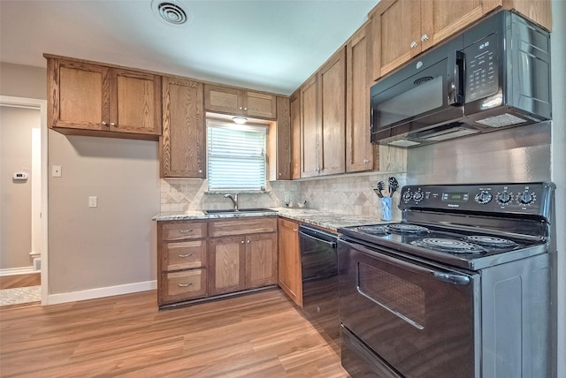 kitchen featuring sink, light stone counters, tasteful backsplash, black appliances, and light wood-type flooring