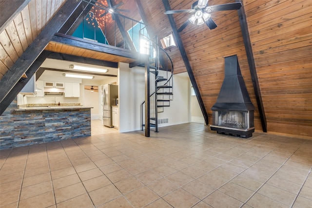 unfurnished living room featuring wood ceiling, a wood stove, high vaulted ceiling, light tile patterned floors, and beam ceiling