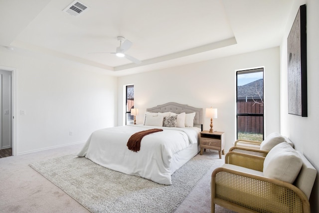 bedroom featuring a raised ceiling, ceiling fan, multiple windows, and carpet flooring