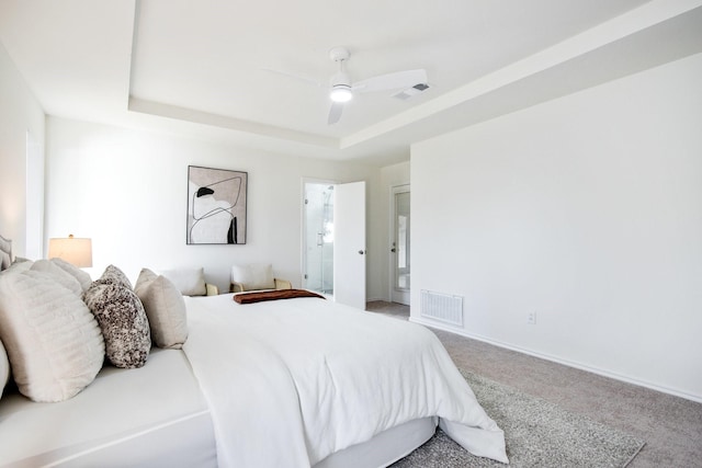 bedroom featuring a raised ceiling, ceiling fan, carpet, and connected bathroom