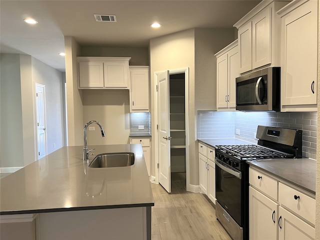 kitchen with stainless steel appliances, white cabinets, a center island with sink, and sink