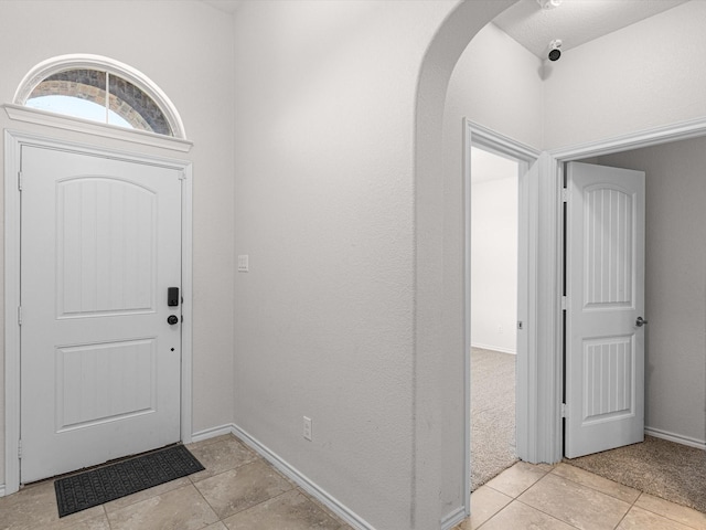 foyer entrance featuring light tile patterned floors, baseboards, and arched walkways