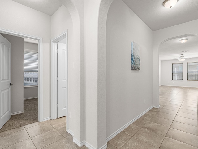 hall with arched walkways, light tile patterned flooring, and baseboards