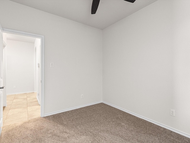 spare room featuring light colored carpet, ceiling fan, baseboards, and light tile patterned floors