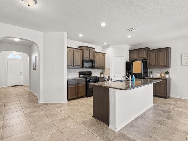 kitchen with arched walkways, a kitchen island with sink, a sink, black appliances, and tasteful backsplash