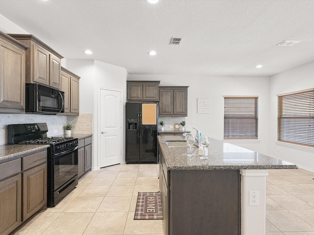 kitchen featuring light tile patterned floors, a sink, visible vents, black appliances, and a center island with sink