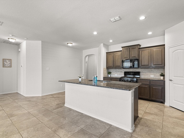 kitchen with visible vents, decorative backsplash, a kitchen island with sink, black appliances, and a sink