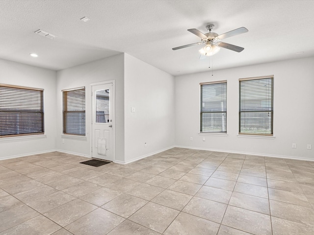 empty room featuring light tile patterned floors, a textured ceiling, visible vents, baseboards, and a ceiling fan