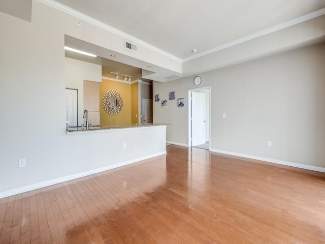 unfurnished living room with track lighting, crown molding, hardwood / wood-style flooring, and sink