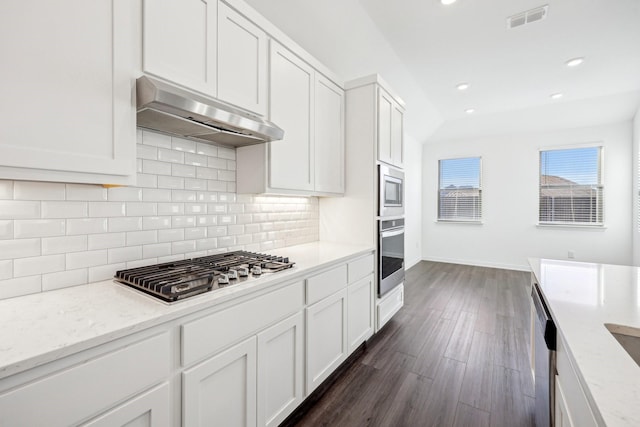 kitchen with appliances with stainless steel finishes, white cabinetry, backsplash, light stone counters, and dark hardwood / wood-style flooring