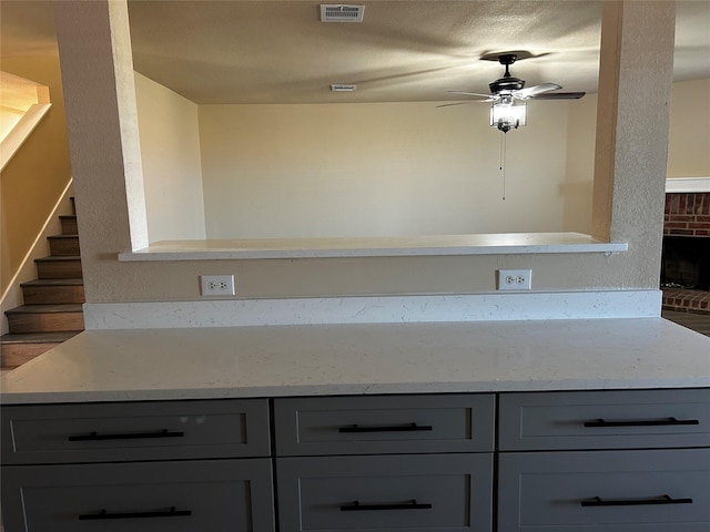 interior space featuring kitchen peninsula, a brick fireplace, ceiling fan, gray cabinetry, and light stone counters