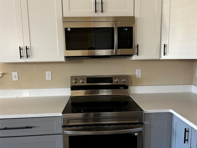 kitchen featuring light stone counters, white cabinets, gray cabinetry, and stainless steel appliances