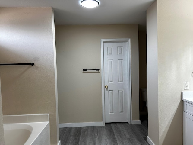 bathroom with hardwood / wood-style flooring, a relaxing tiled tub, toilet, and vanity