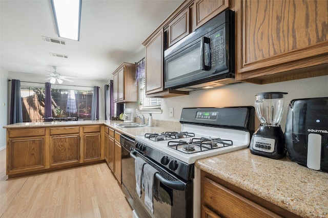 kitchen with light hardwood / wood-style floors, ceiling fan, light stone countertops, black appliances, and sink