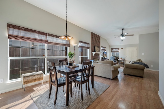 dining space featuring hardwood / wood-style flooring, a brick fireplace, ceiling fan, and vaulted ceiling