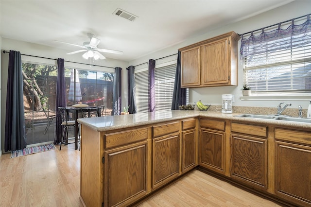 kitchen with ceiling fan, sink, kitchen peninsula, and light wood-type flooring