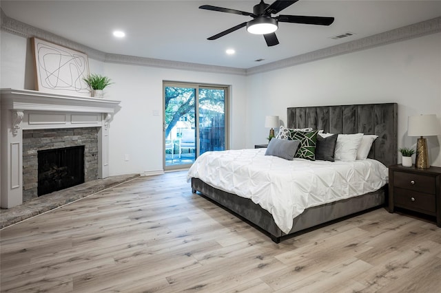 bedroom featuring crown molding, access to exterior, a stone fireplace, and light hardwood / wood-style flooring