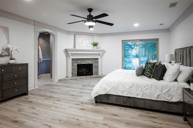 bedroom with a stone fireplace, access to exterior, ceiling fan, crown molding, and light wood-type flooring