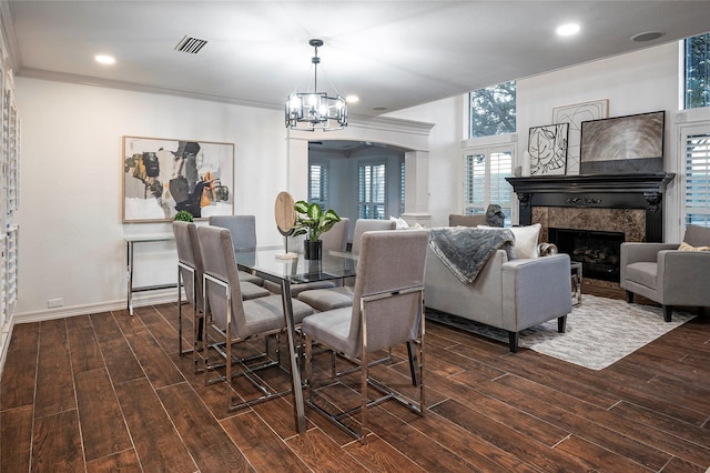 dining space featuring dark wood-type flooring, a high end fireplace, crown molding, and an inviting chandelier