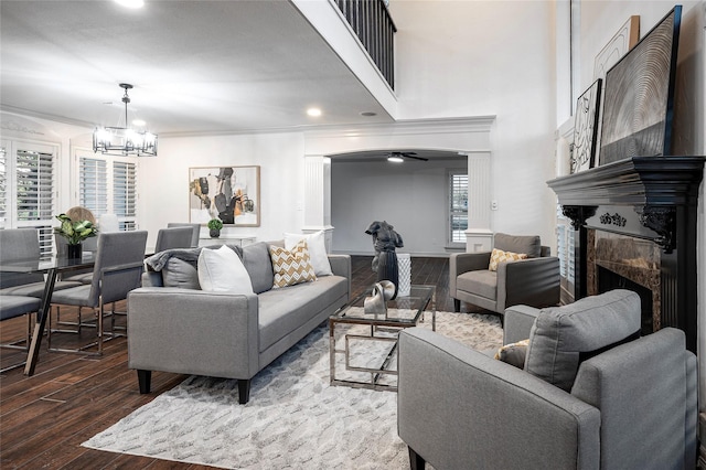 living room featuring crown molding, hardwood / wood-style floors, a high ceiling, a fireplace, and ceiling fan with notable chandelier