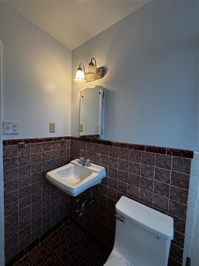 bathroom featuring toilet, tile walls, and sink