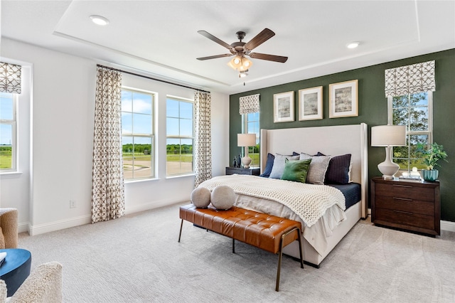 bedroom with ceiling fan, a tray ceiling, and light colored carpet