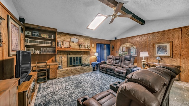 living room featuring ceiling fan, a brick fireplace, wood walls, vaulted ceiling with beams, and a textured ceiling