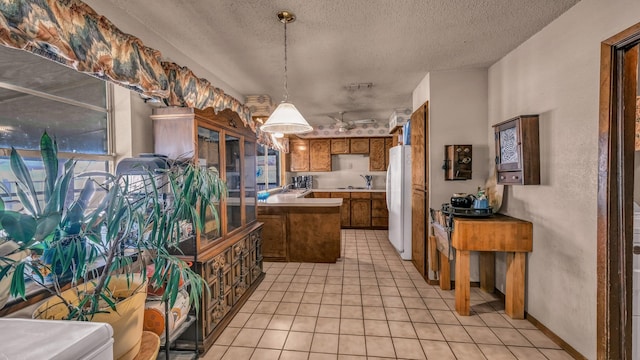 kitchen featuring light tile patterned floors, decorative light fixtures, a textured ceiling, white refrigerator, and sink