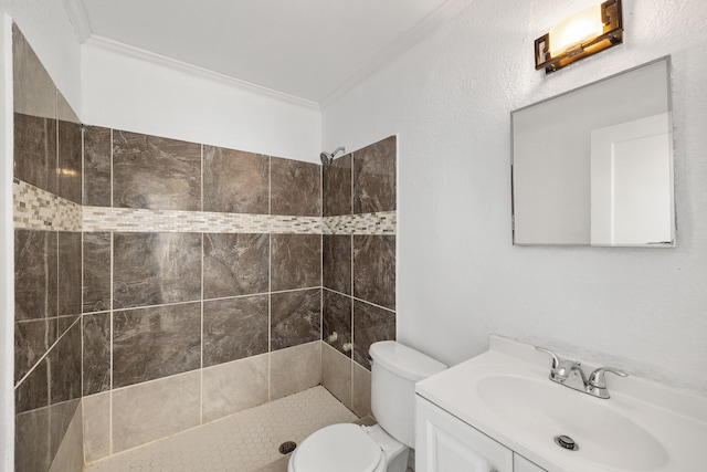 bathroom featuring a tile shower, toilet, vanity, and crown molding