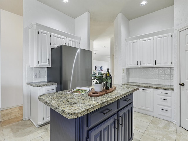 kitchen with decorative backsplash, white cabinets, light stone counters, and a center island